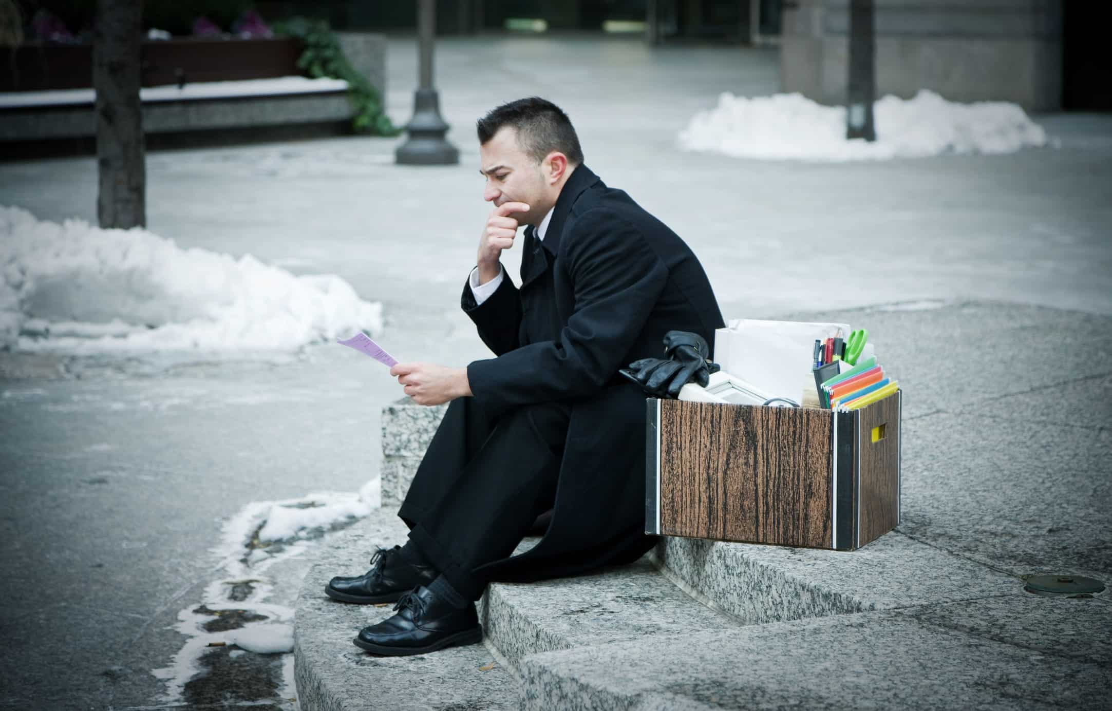 worried man sitting on the sidewalk looking at documents